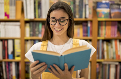 Joven mujer sonriente leyendo un libro en la biblioteca