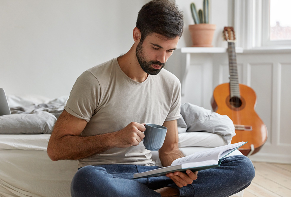 Hombre leyendo un libro, mientras bebe una aromática